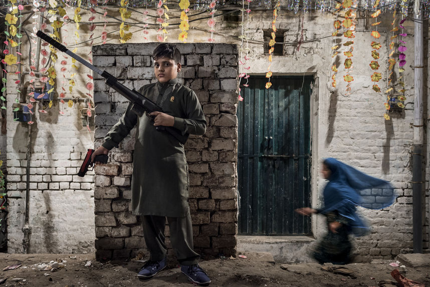 On the eve of religious celebration, a gracious blue shadow floats by a boy boasting his toy guns